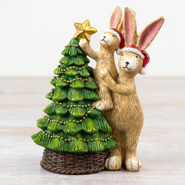 Decorative figurine of two rabbits with a Christmas tree on a light wooden surface