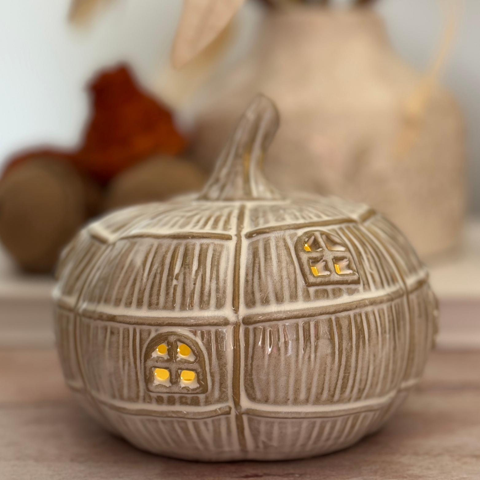 Decorative ceramic pumpkin with a house design and small light inside, on a wooden surface.
