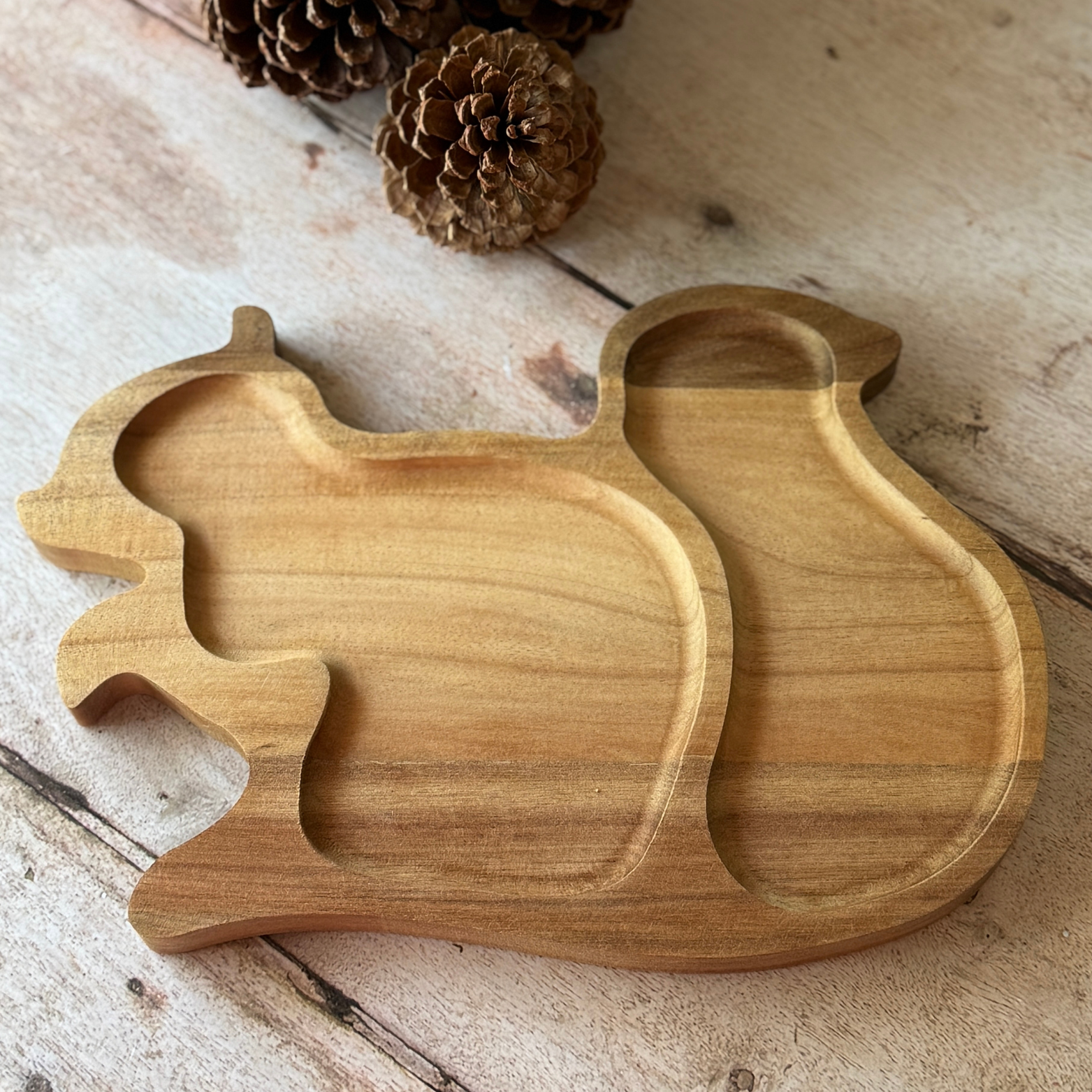 Wooden squirrel-shaped tray on a wooden surface with pine cones.