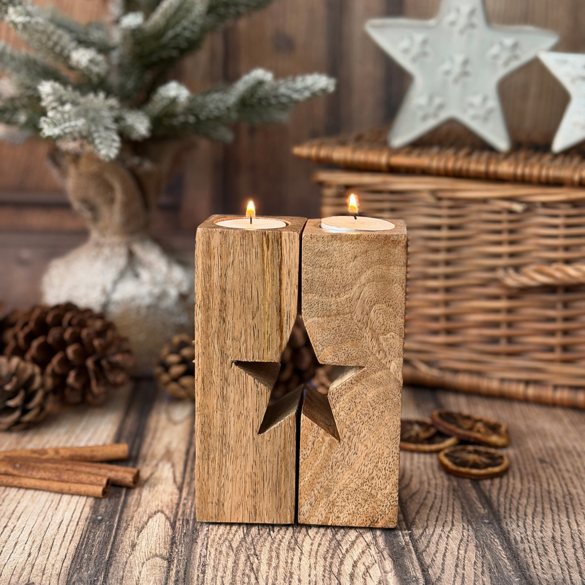 A rustic wooden candle holder with a carved star cutout, holding two lit tea lights, styled on a wooden surface with pinecones, cinnamon sticks, and holiday decorations in the background.