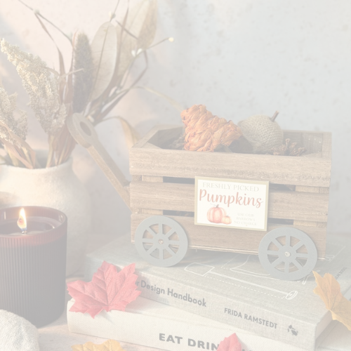 A small square wooden picture frame sign with a humorous quote about hot chocolate, displayed on a rustic wooden table with a mug, flowers, and a candle in the background.