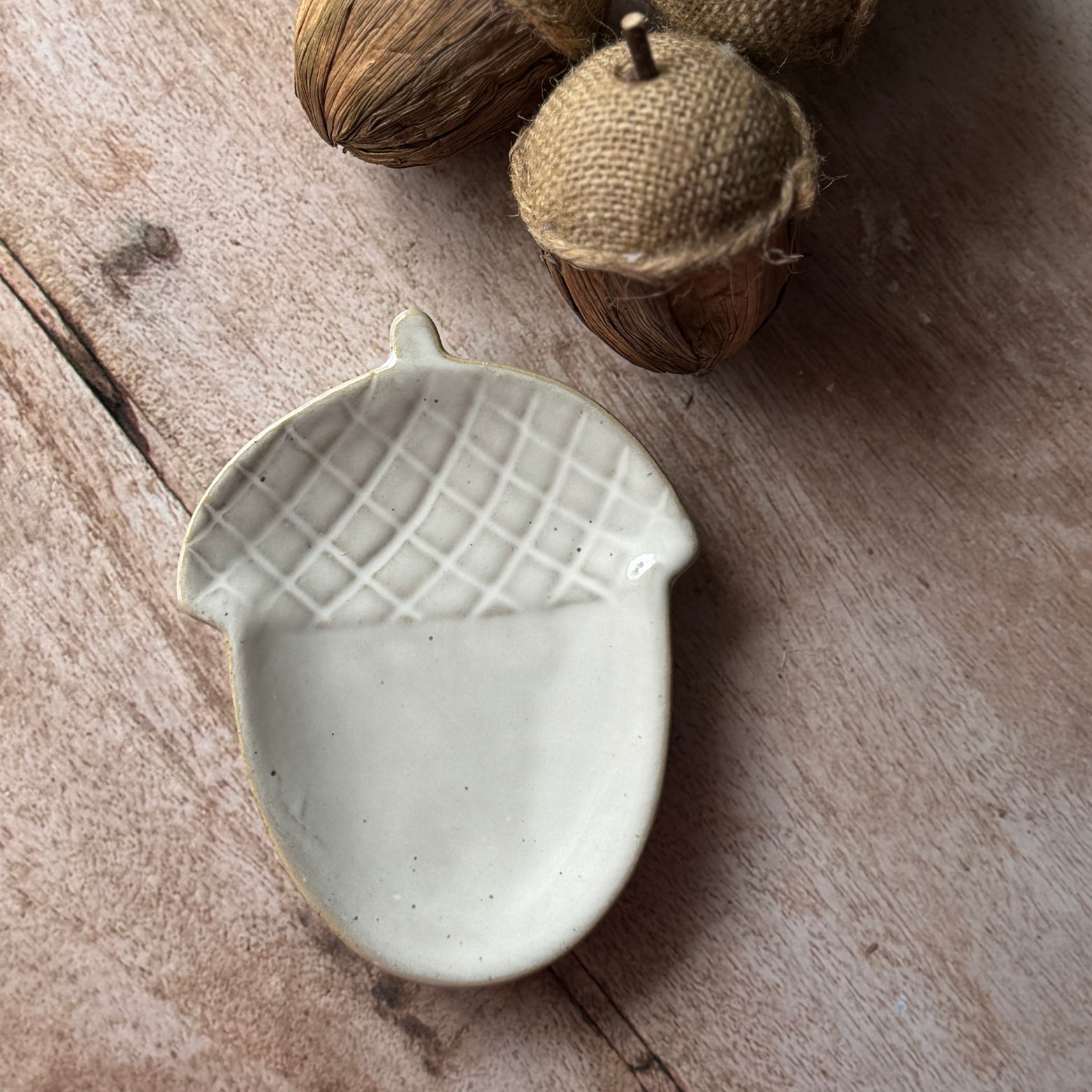 Ceramic acorn-shaped dish on a wooden surface with acorns in the background