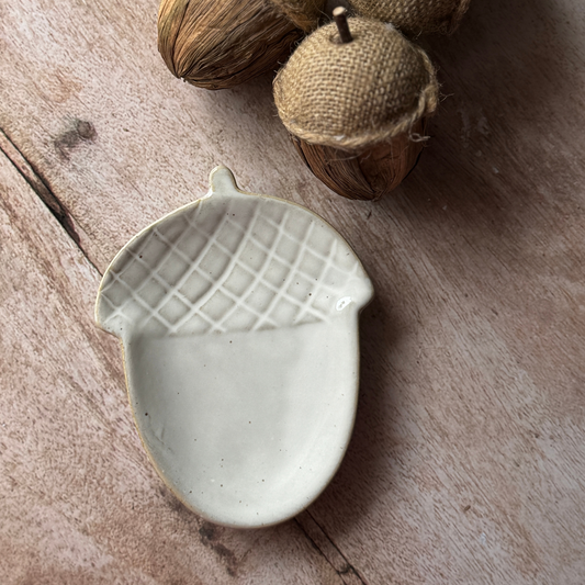 Ceramic acorn-shaped dish on a wooden surface with acorns in the background