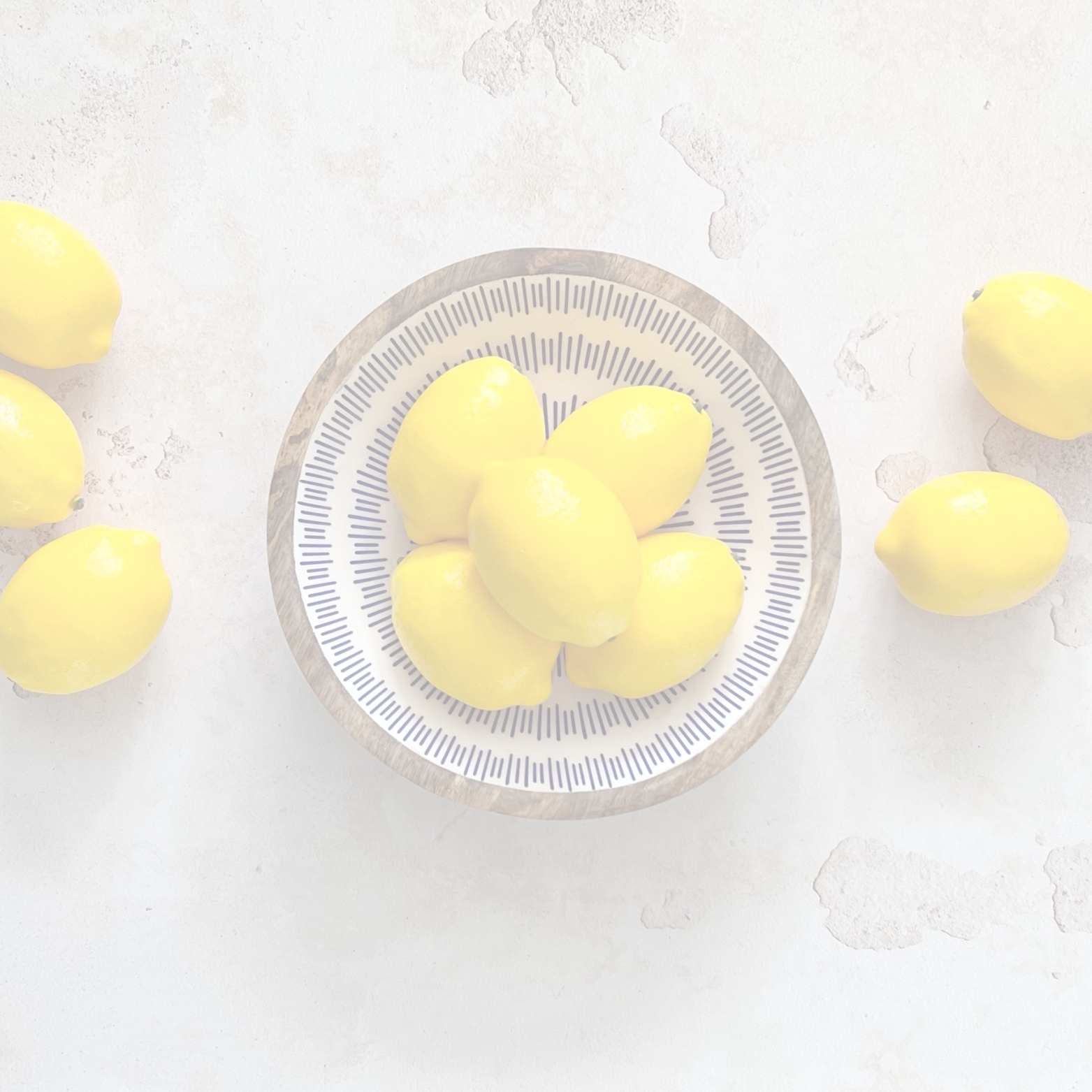 Yellow lemons in a white and blue bowl with lemons scattered around on a light grey background