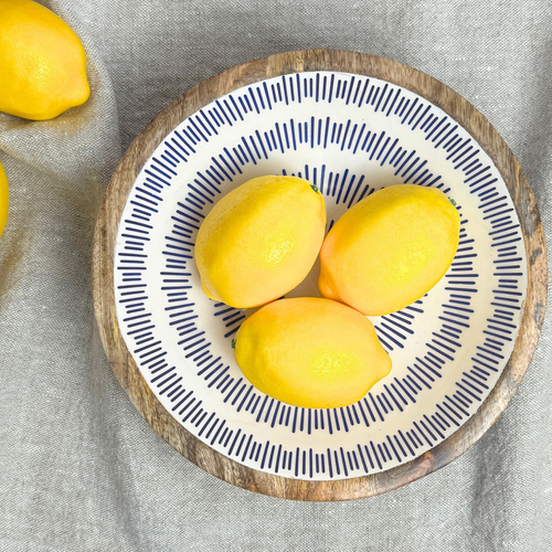 Three lemons in a decorative bowl with a blue stripe pattern on a gray fabric background