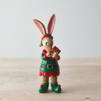 Decorative figurine of a rabbit dressed as an elf holding a gift on a wooden surface.