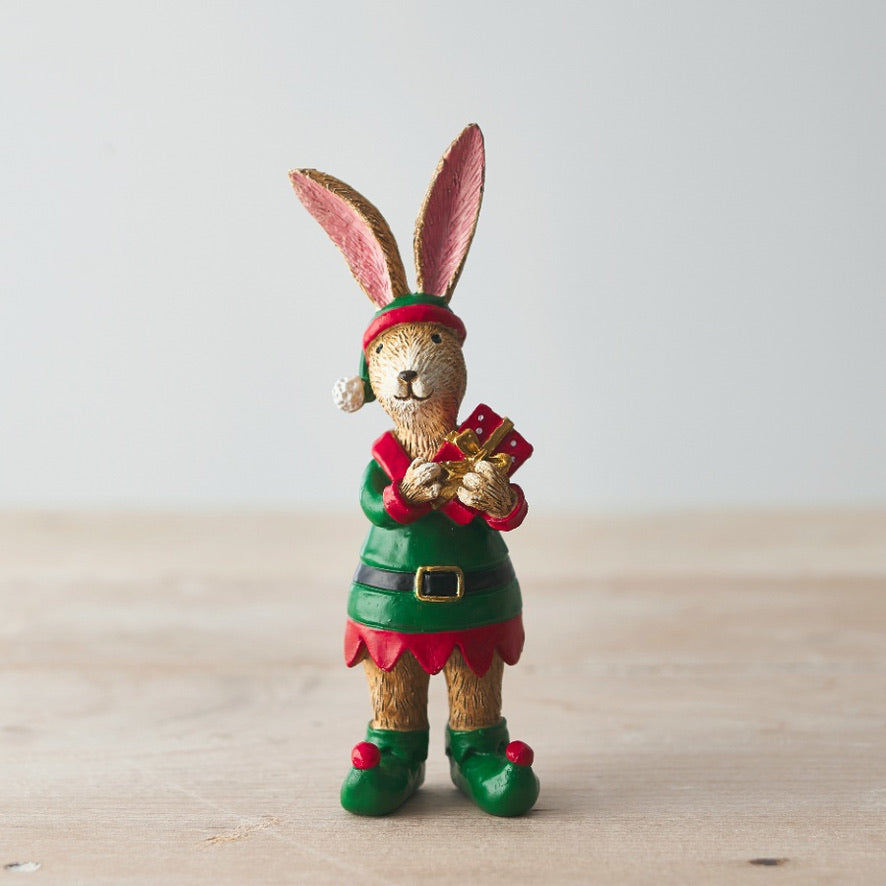 Decorative figurine of a rabbit dressed as an elf holding a gift on a wooden surface.