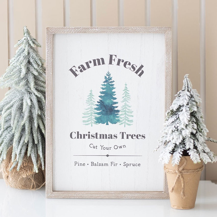 Framed sign with 'Farm Fresh Christmas Trees' text and tree illustrations, surrounded by small potted trees.