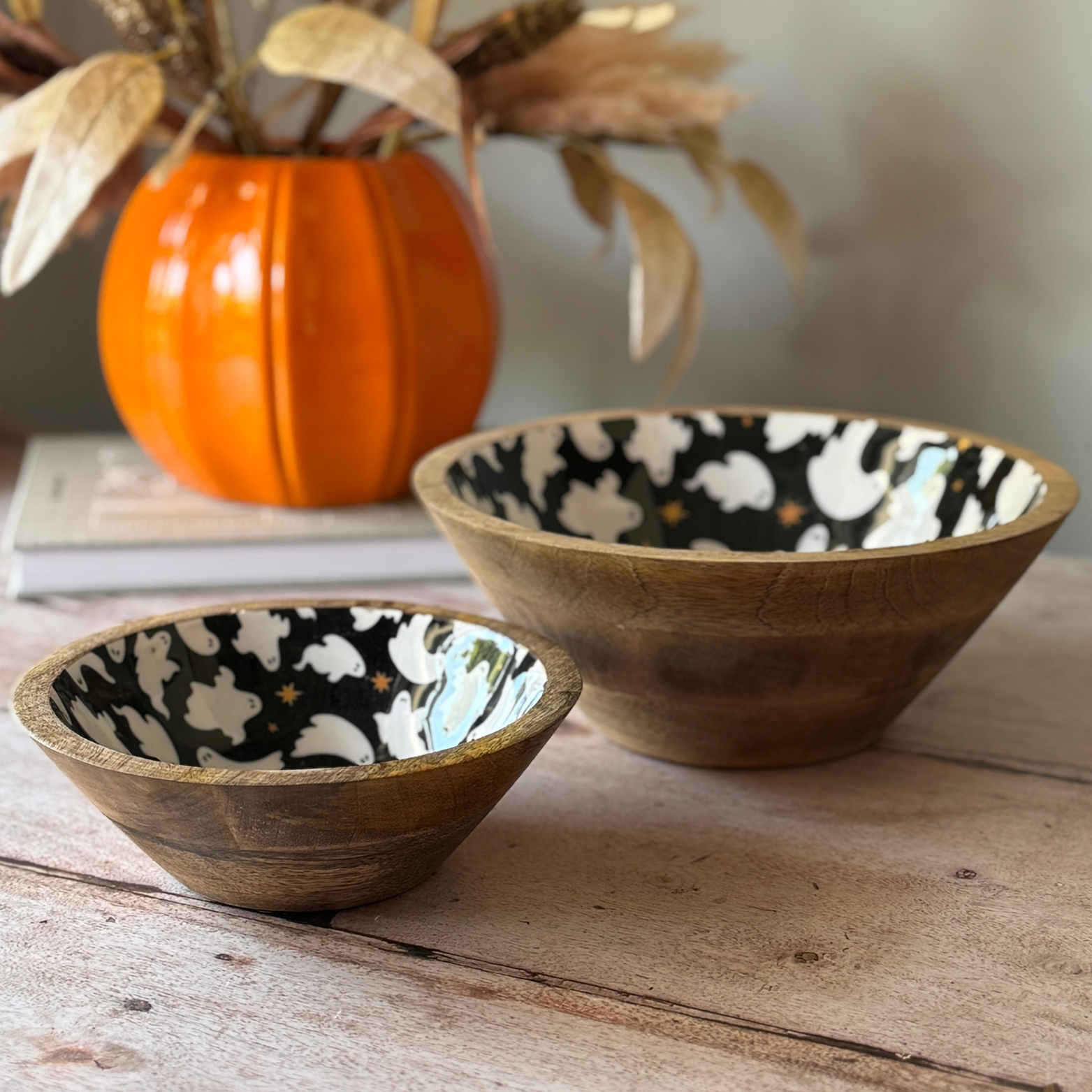 Two wooden bowls black inside with ghost pattern on a wooden surface with a pumpkin in the background.