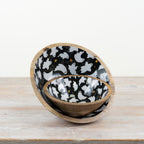 Wooden bowl with black interior featuring white ghost patterns on a wooden surface.