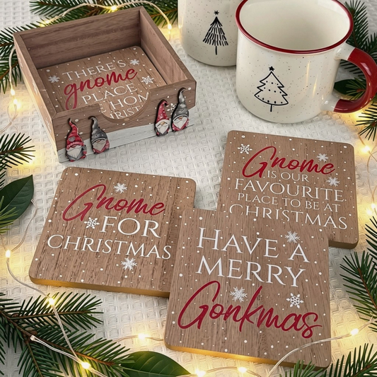 A set of Christmas gnome-themed wooden coasters and a matching wooden box, styled with pine branches, warm fairy lights, and white speckled mugs on a textured white surface.