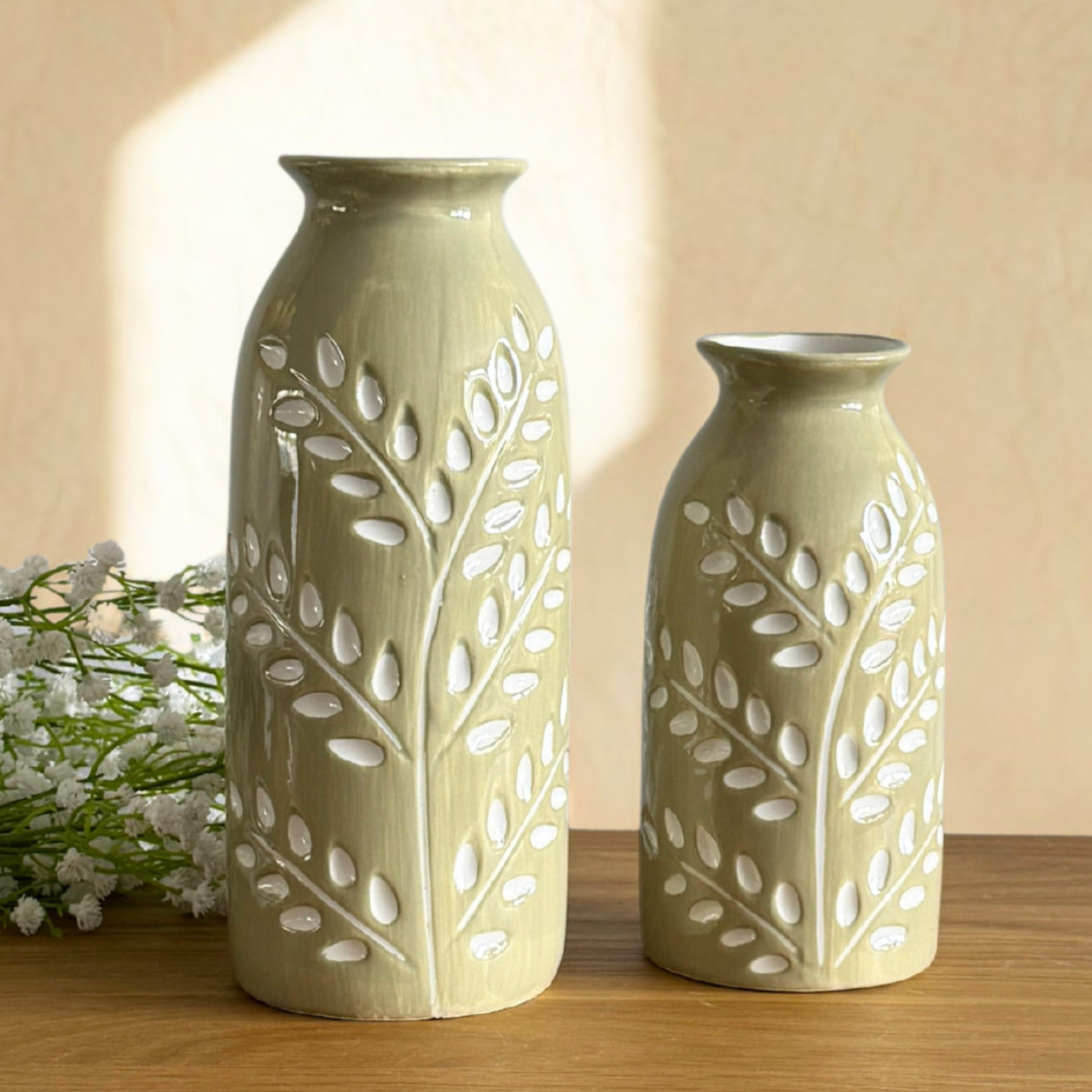 Two ceramic vases with leaf patterns on a wooden surface.