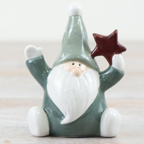 Small green santa figurine holding a red star on a light wooden surface