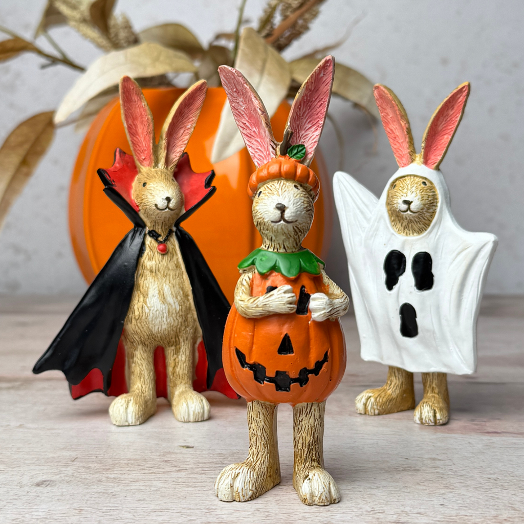 Three rabbit figurines dressed in Halloween costumes against a neutral background