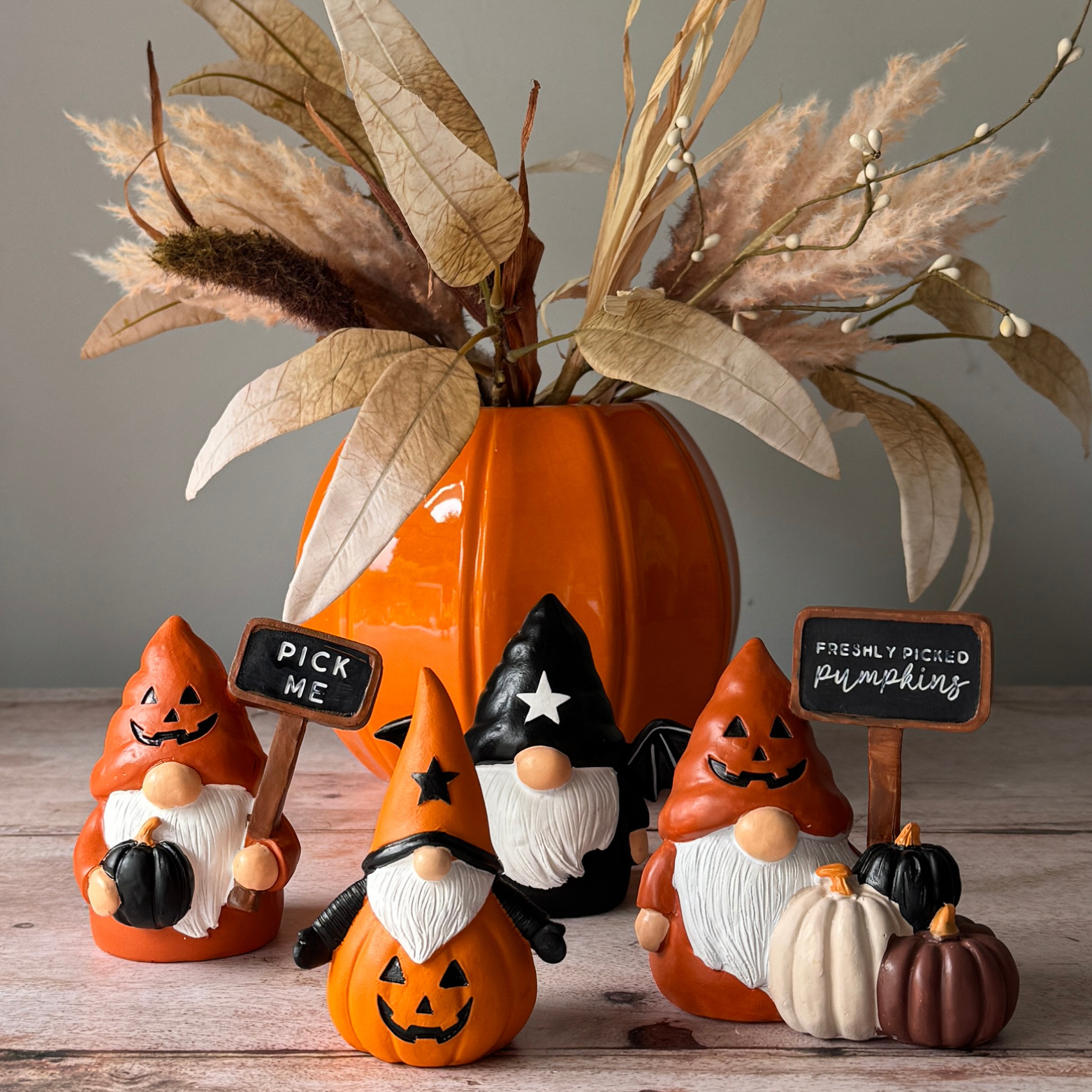 Halloween-themed gnomes and pumpkins with decorative elements on a wooden surface.