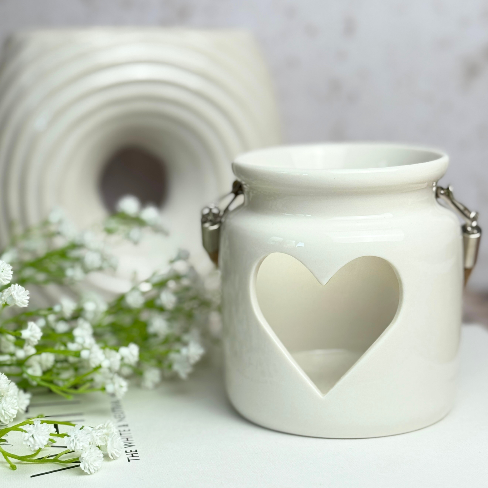 White ceramic lantern with heart cutout and small white flowers on a light background