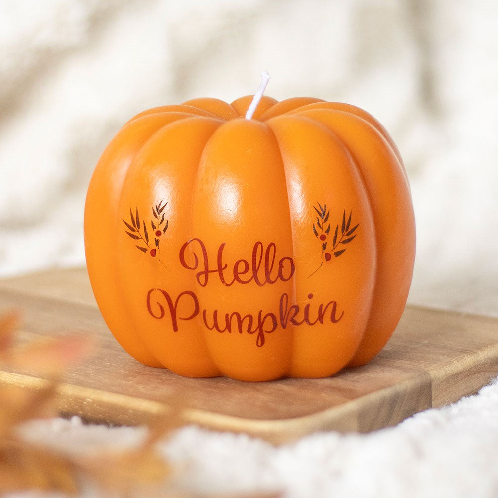 Pumpkin-shaped candle with 'Hello Pumpkin' text on a wooden surface