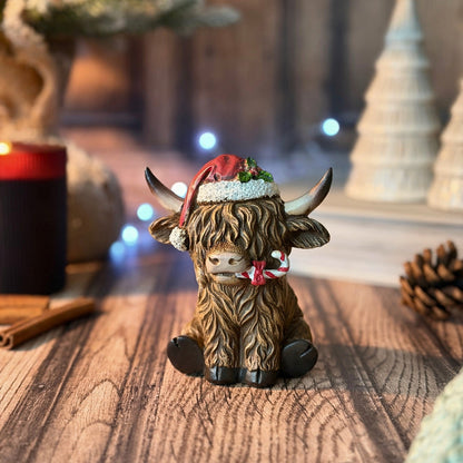 A Highland cow figurine decorated with a red Santa hat and a red-and-white candy cane, sitting on a wooden surface with a warm, festive background.