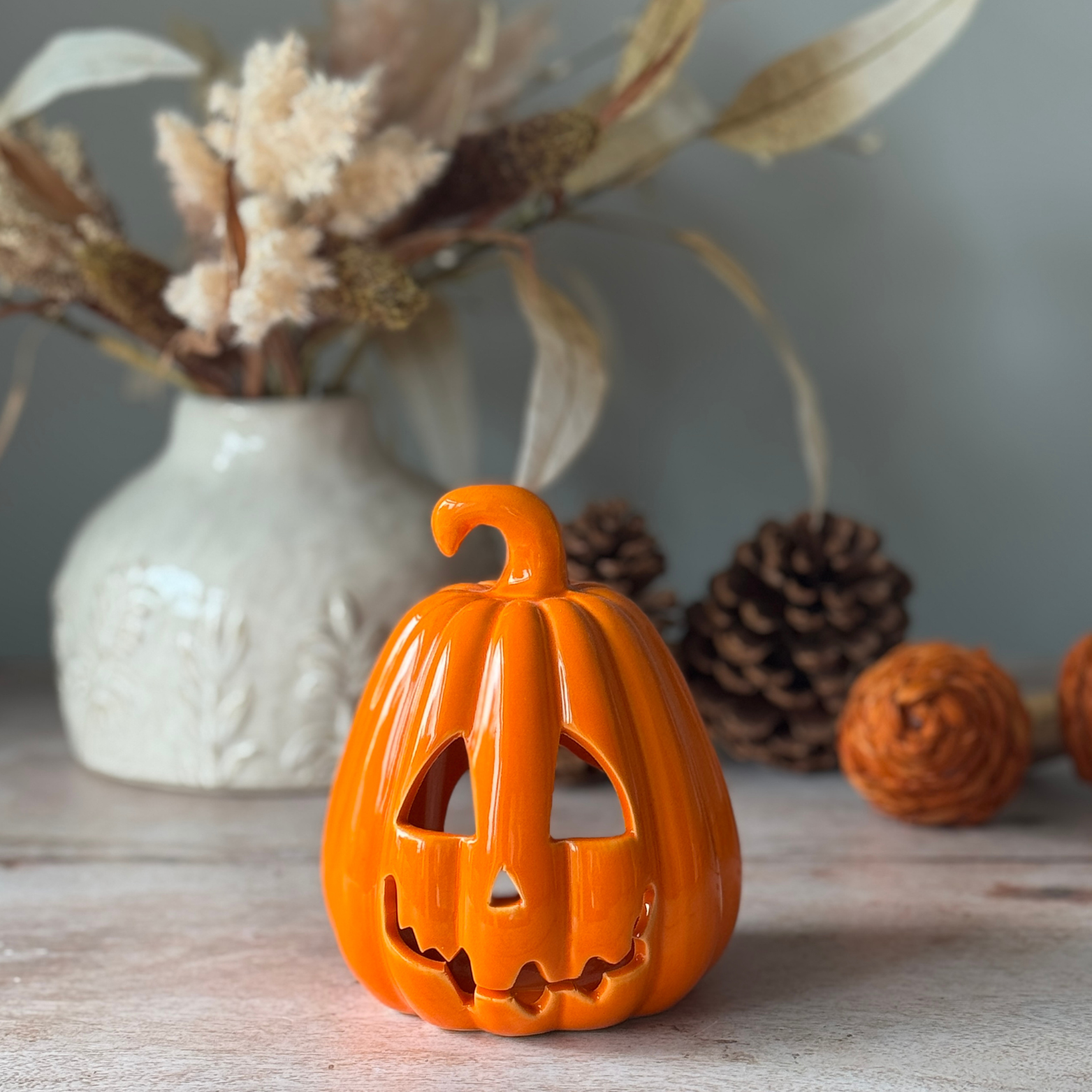 Orange ceramic jack-o'-lantern on a wooden surface with decorative elements in the background.