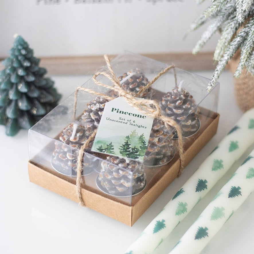 Set of pinecone candles in a clear box with a decorative bow, surrounded by Christmas decor.