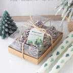 Set of pinecone candles in a clear box with a decorative bow, surrounded by Christmas decor.