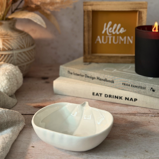 A small white ceramic bowl with a textured, ribbed exterior and a pointed bottom, styled on a rustic wooden table with books, a candle, and a decorative sign in the background.