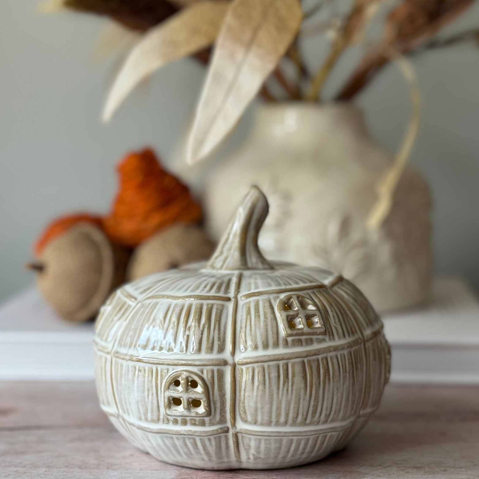 Decorative ceramic pumpkin with textured surface and small windows, placed on a neutral background.