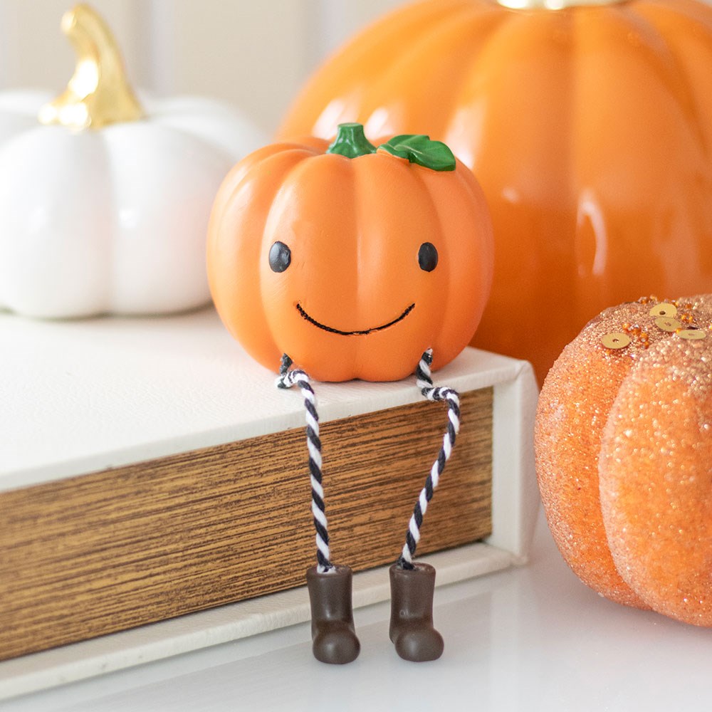 Decorative pumpkin with a face and legs on a shelf with other pumpkins in the background.
