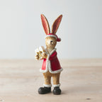 Decorative rabbit figurine in a Santa outfit holding a gift on a wooden surface.