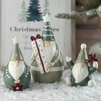 Three decorative santas with green hats and white beards on a snowy surface.