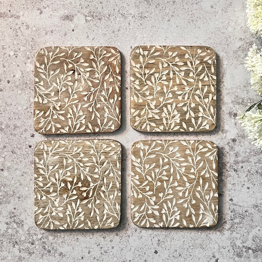 Four square coasters with leaf patterns on a textured surface