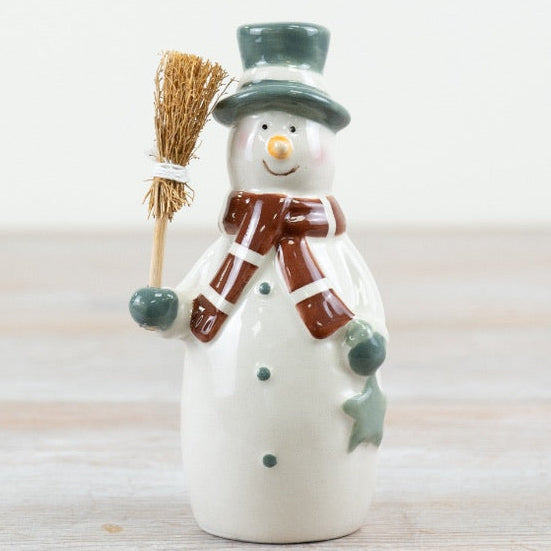 Ceramic snowman figurine with a broom, green hat and brown scarf.