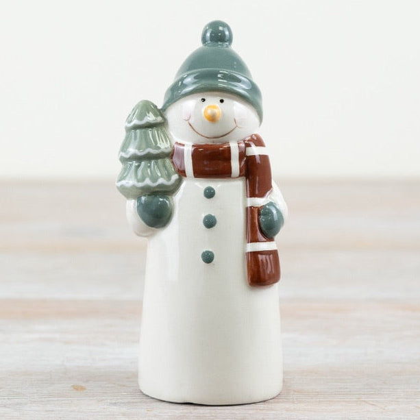 Small ceramic snowman figurine with a green hat and brown scarf holding a tree