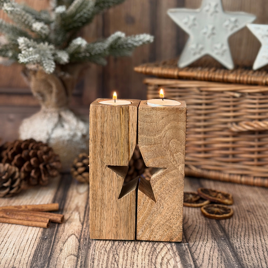 A rustic wooden candle holder with a carved star cutout, holding two lit tea lights, styled on a wooden surface with pinecones, cinnamon sticks, and holiday decorations in the background.