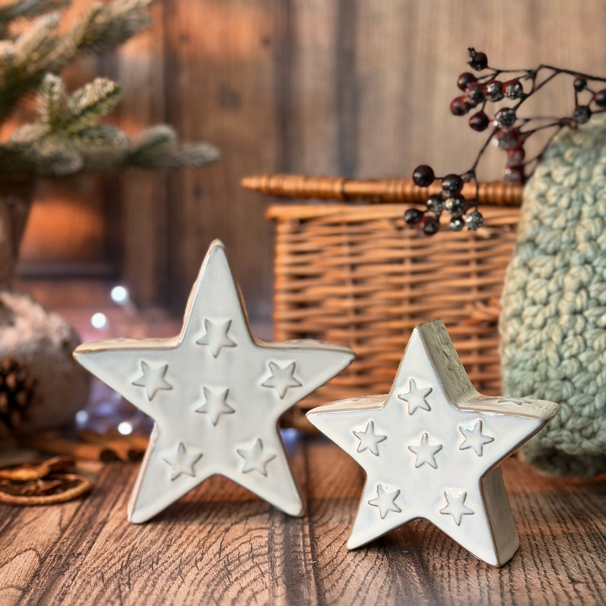 Two white ceramic stars with embossed star patterns, displayed on a rustic wooden surface with holiday decorations in the background.