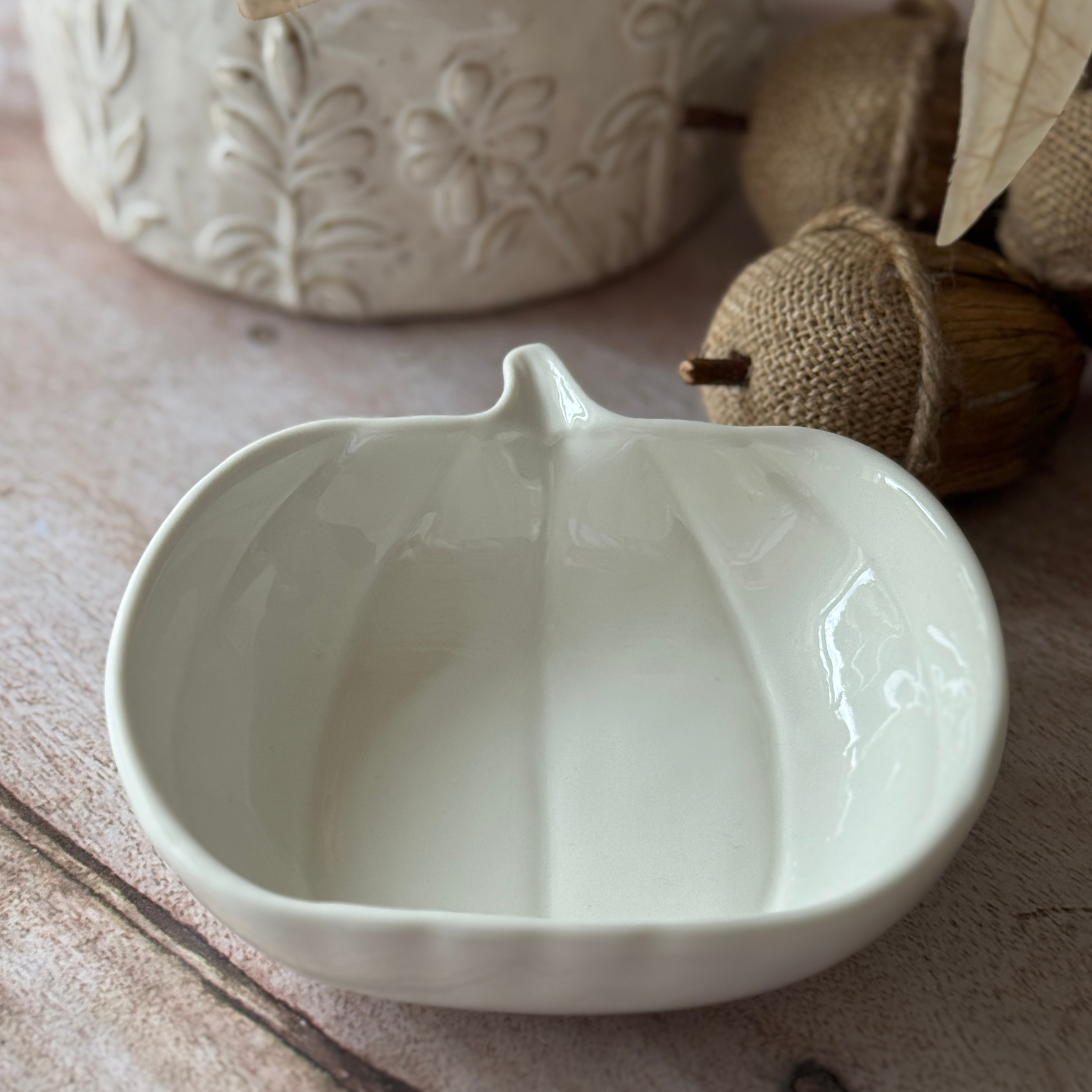White ceramic pumpkin-shaped bowl on a wooden surface with decorative elements.